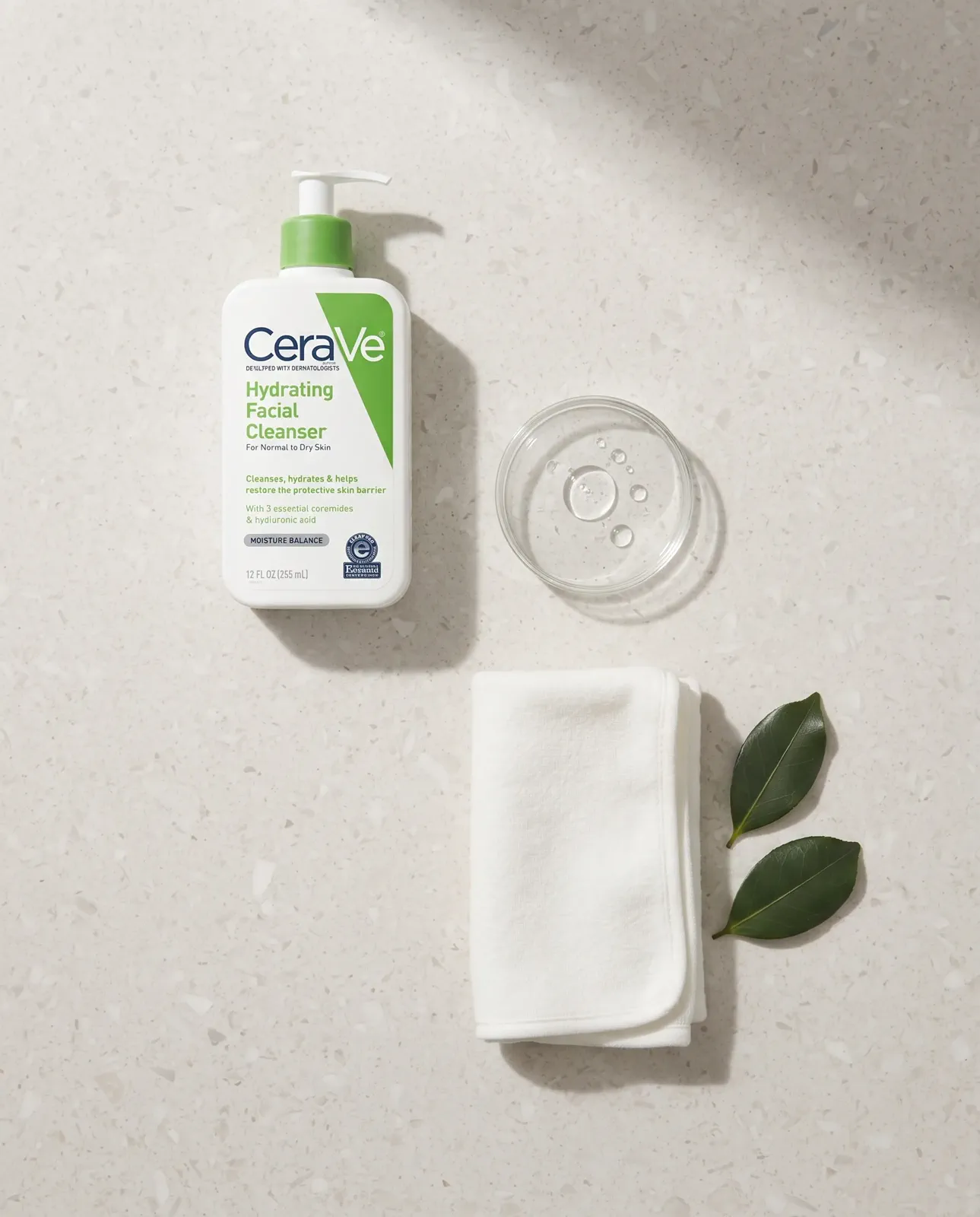 A top-down skincare routine with the cleanser as the clear focal point and supporting bathroom objects arranged around it.