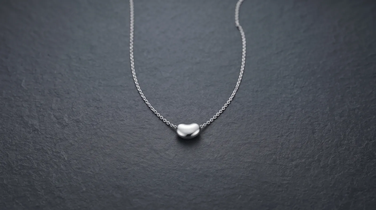 A silver pendant kept complete and centered against dark stone with controlled edge highlights.